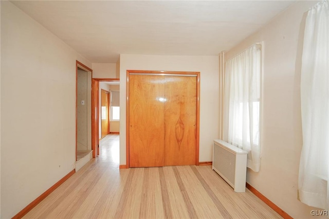 unfurnished bedroom featuring radiator, light wood-style flooring, and baseboards