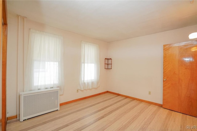 empty room featuring light wood-type flooring, radiator, and baseboards