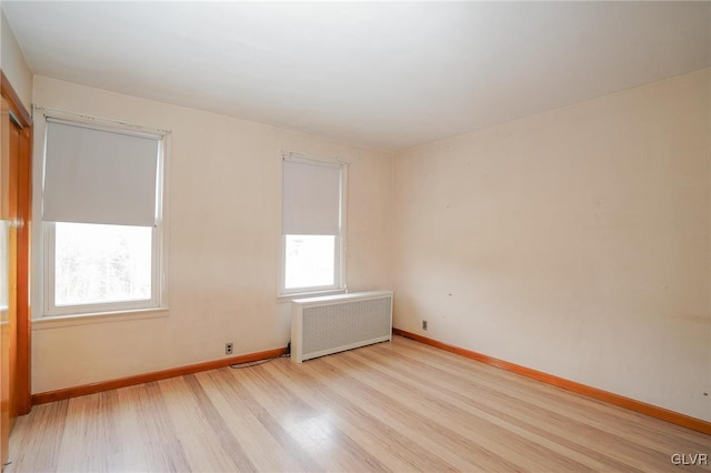 unfurnished room with radiator heating unit, light wood-type flooring, and baseboards