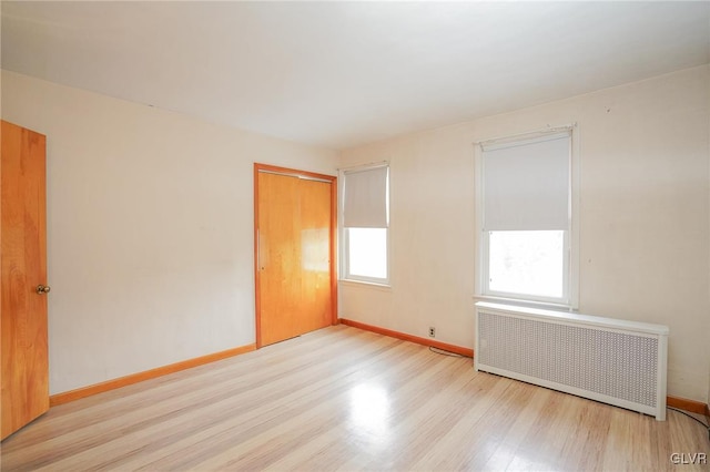 unfurnished room with radiator heating unit, light wood-style flooring, and baseboards