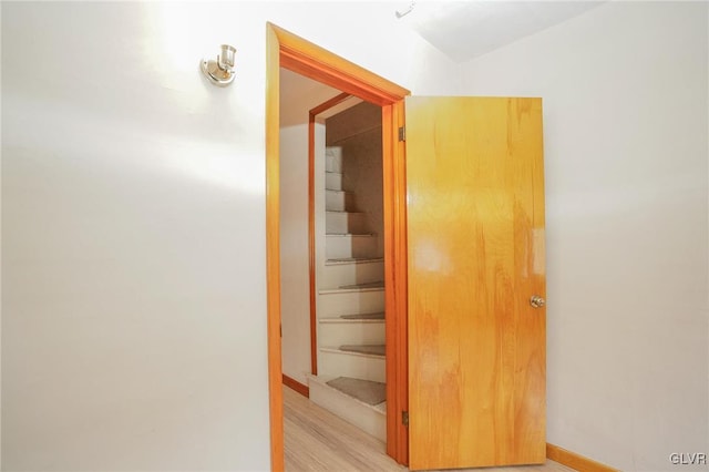 corridor with light wood finished floors, baseboards, and stairway