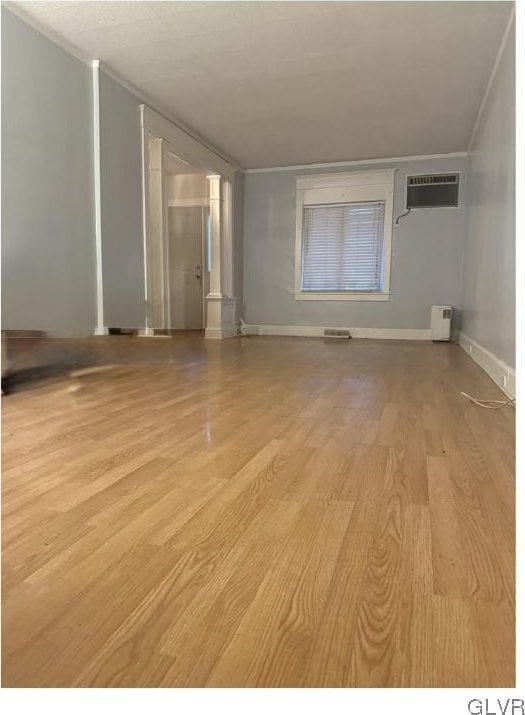 unfurnished room with light wood finished floors, baseboards, and an AC wall unit