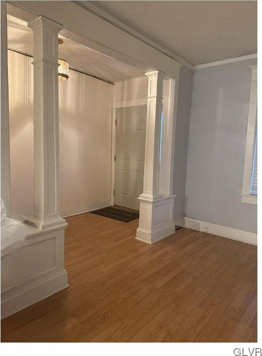 empty room featuring ornate columns, baseboards, and wood finished floors