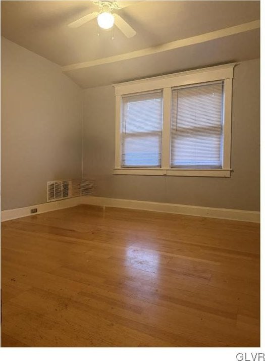 unfurnished room with lofted ceiling, wood finished floors, visible vents, and baseboards