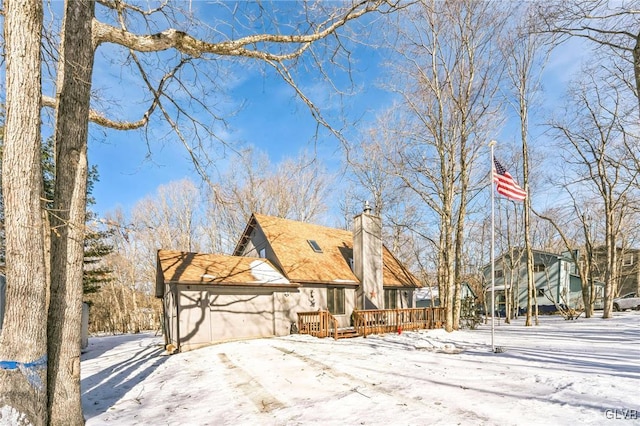 view of snowy exterior with an attached garage, a chimney, and a wooden deck