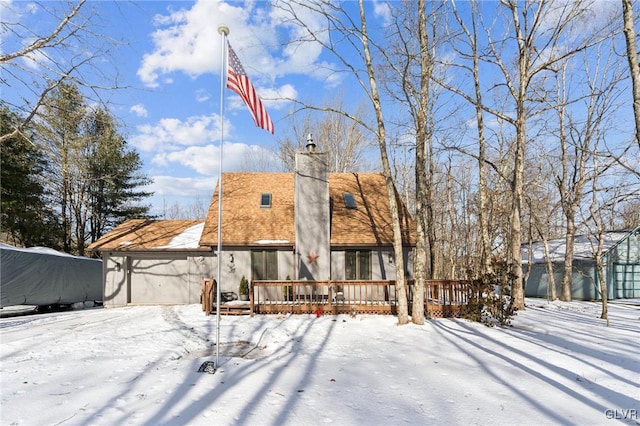 snow covered back of property with a chimney and a wooden deck