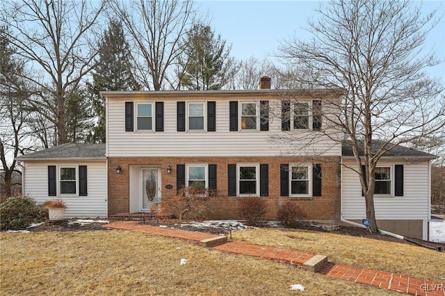 view of front facade featuring a front lawn, a chimney, and brick siding