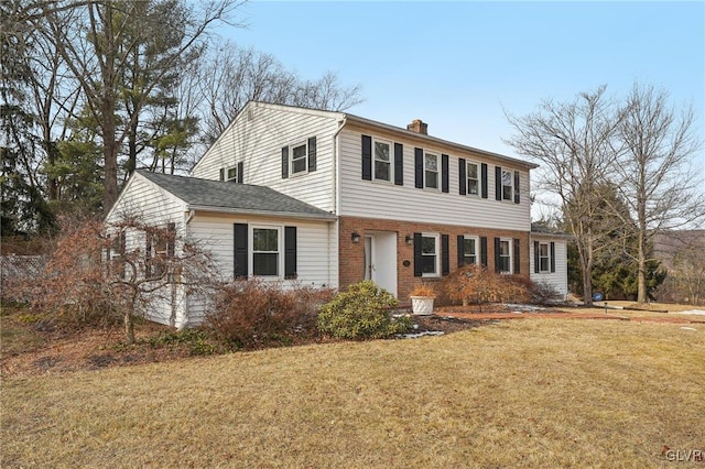 colonial inspired home featuring brick siding, a chimney, and a front yard