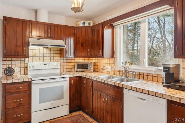 kitchen with under cabinet range hood, white appliances, a sink, tile counters, and tasteful backsplash