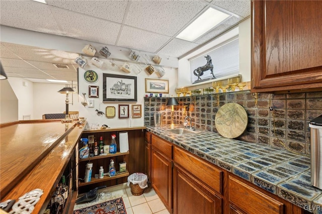 bar with indoor wet bar, light tile patterned floors, tasteful backsplash, a sink, and a drop ceiling