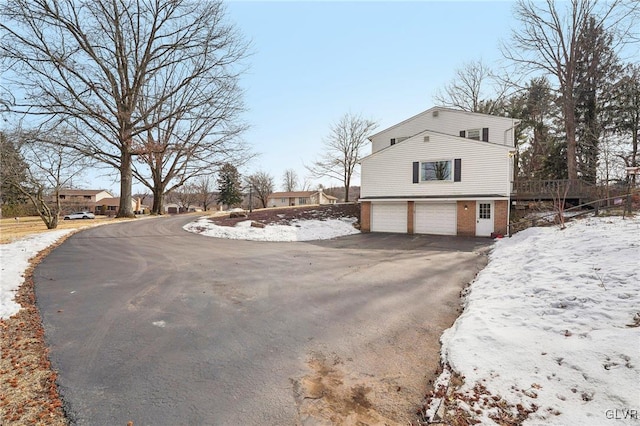 view of snow covered exterior with a garage, a residential view, aphalt driveway, and brick siding