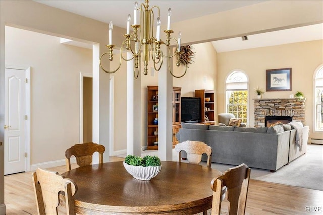 dining area featuring an inviting chandelier, a fireplace, light wood-type flooring, and baseboards