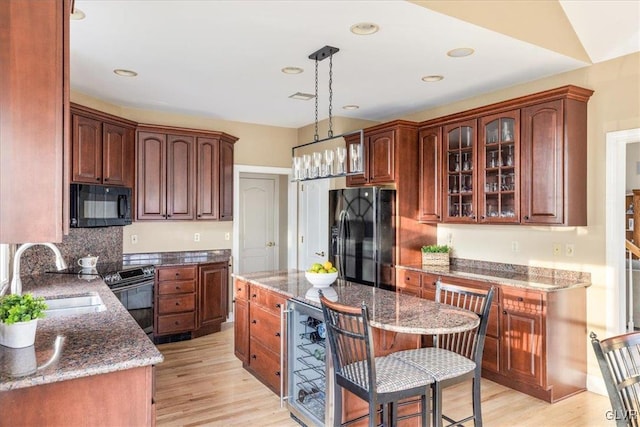 kitchen with a sink, black appliances, a center island, and light wood finished floors