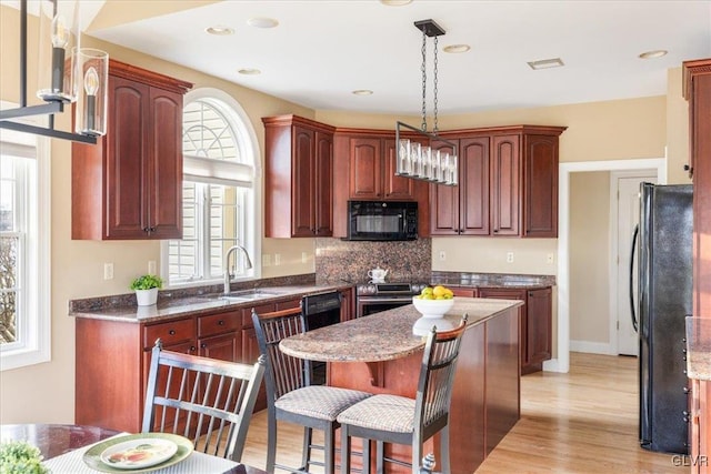 kitchen with a kitchen bar, black appliances, a sink, a center island, and light wood-style floors