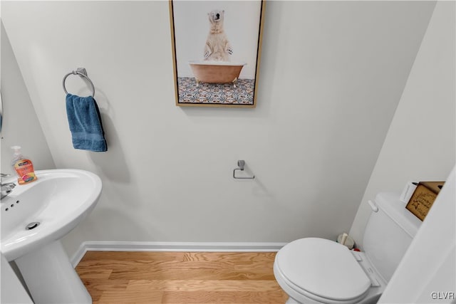 half bathroom with a sink, wood finished floors, toilet, and baseboards