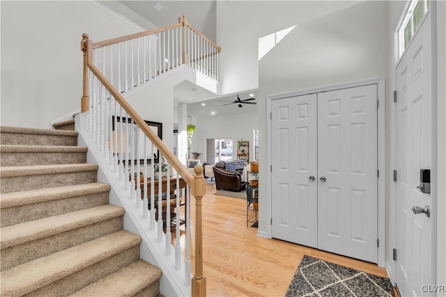 foyer entrance with a skylight, wood finished floors, a towering ceiling, a ceiling fan, and stairway