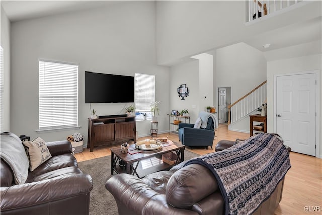 living room with light wood-type flooring, baseboards, stairway, and a high ceiling