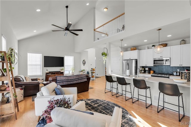 living area with a ceiling fan, recessed lighting, high vaulted ceiling, and light wood-style flooring