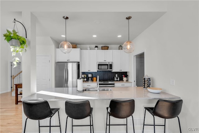 kitchen with light stone counters, white cabinetry, hanging light fixtures, appliances with stainless steel finishes, and backsplash