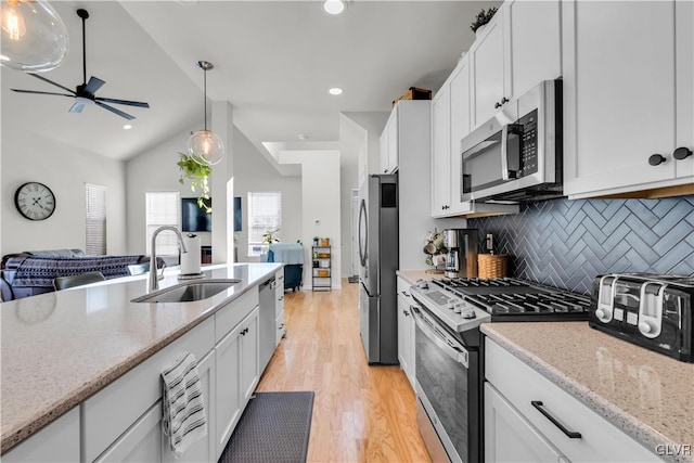 kitchen with a sink, white cabinets, open floor plan, hanging light fixtures, and appliances with stainless steel finishes