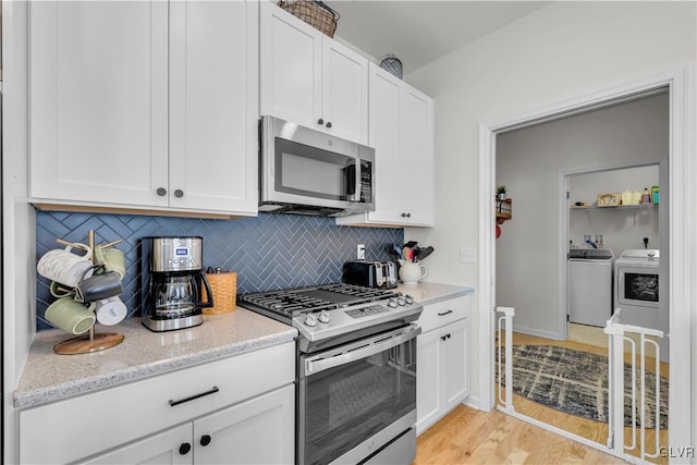 kitchen featuring washing machine and dryer, stainless steel appliances, white cabinetry, light stone countertops, and tasteful backsplash