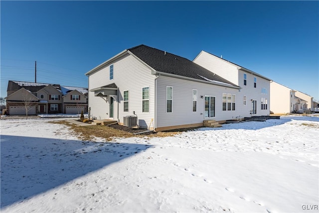 snow covered rear of property featuring entry steps, central AC unit, and a residential view