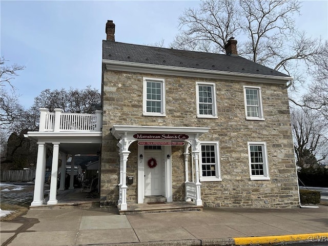 view of front of property featuring stone siding, a chimney, and a balcony