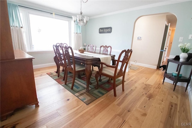 dining room with light wood-style floors, baseboards, arched walkways, and crown molding