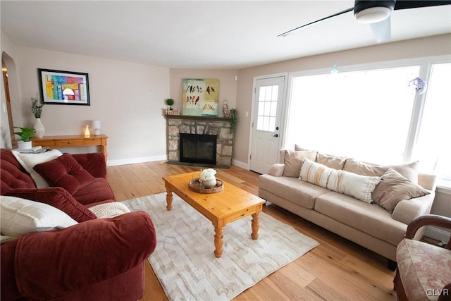 living room with arched walkways, a fireplace, light wood-style floors, a ceiling fan, and baseboards