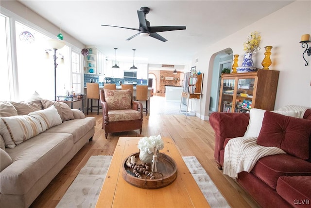 living area featuring arched walkways, light wood finished floors, and a ceiling fan