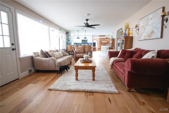 living area featuring arched walkways, visible vents, light wood-type flooring, and a ceiling fan