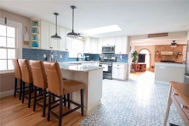 kitchen featuring a breakfast bar, open shelves, appliances with stainless steel finishes, white cabinetry, and a peninsula