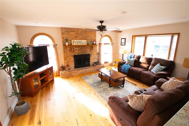 living room featuring a healthy amount of sunlight, light wood-type flooring, a fireplace, and a ceiling fan