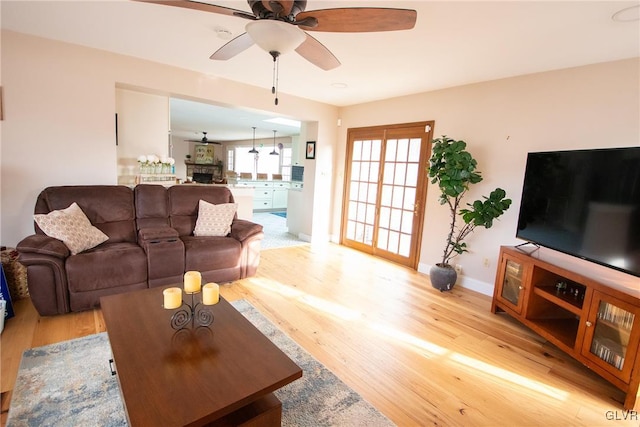 living area featuring light wood-type flooring, ceiling fan, a fireplace, and baseboards