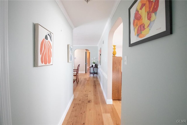 hallway with arched walkways, baseboards, light wood-style flooring, and crown molding