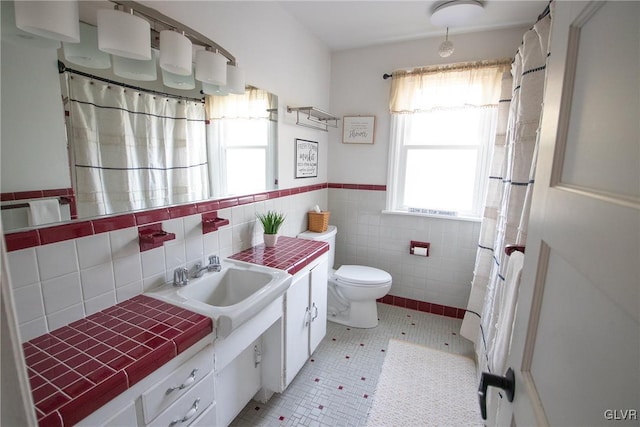 full bathroom featuring toilet, tile walls, vanity, wainscoting, and tile patterned floors