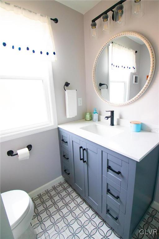 half bath with toilet, tile patterned flooring, vanity, and baseboards