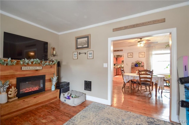 living area featuring a glass covered fireplace, crown molding, and wood finished floors