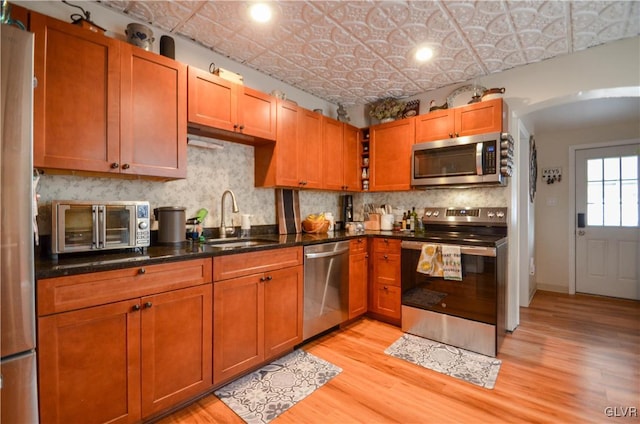 kitchen featuring stainless steel appliances, a sink, light wood-style floors, decorative backsplash, and an ornate ceiling