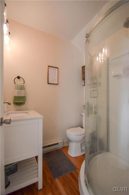 full bath featuring lofted ceiling, a baseboard radiator, toilet, wood finished floors, and a shower stall