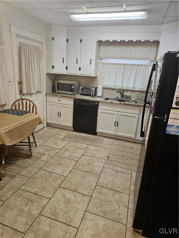 kitchen with a drop ceiling, a toaster, a sink, white cabinetry, and black appliances