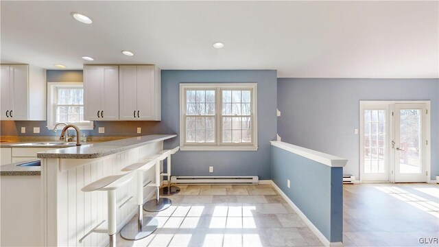 kitchen with recessed lighting, baseboard heating, white cabinets, a sink, and baseboards