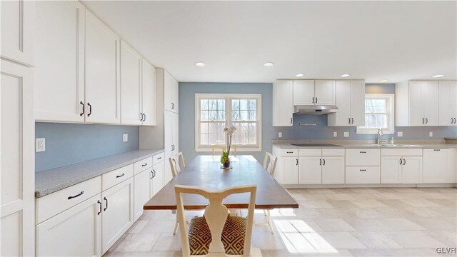 kitchen with white cabinets, black electric stovetop, light countertops, under cabinet range hood, and a sink