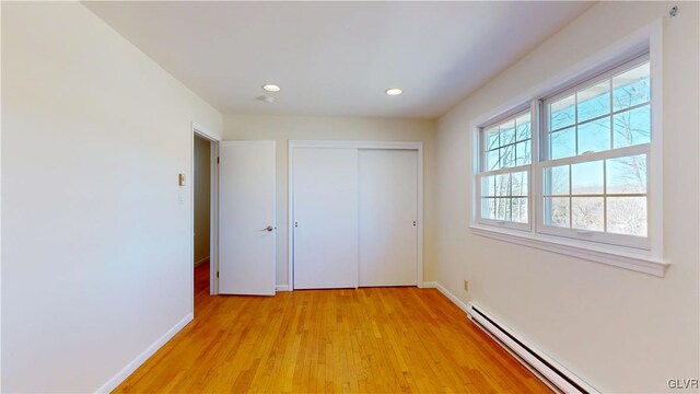 unfurnished bedroom featuring a baseboard radiator, light wood-style flooring, recessed lighting, baseboards, and a closet