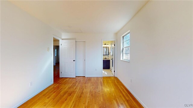 unfurnished bedroom featuring ensuite bathroom, light wood finished floors, attic access, and baseboards