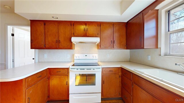 kitchen with white range with electric stovetop, a peninsula, light countertops, under cabinet range hood, and a sink