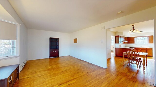 unfurnished dining area with light wood-type flooring, a baseboard heating unit, and a notable chandelier