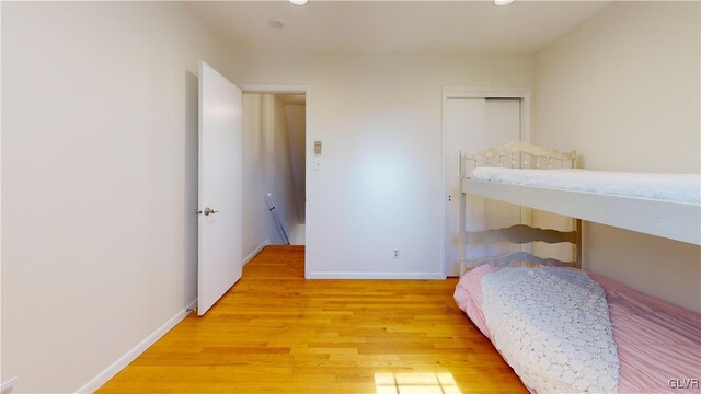 bedroom with light wood-type flooring, a closet, and baseboards