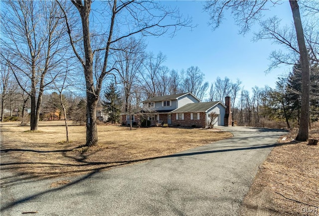 view of home's exterior with a garage, a lawn, a chimney, aphalt driveway, and brick siding