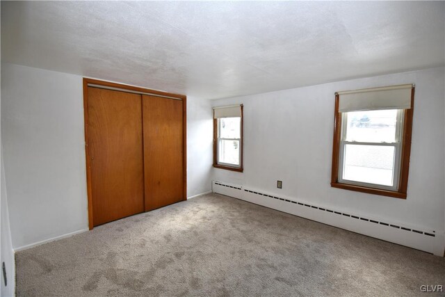 unfurnished bedroom with a closet, baseboard heating, and carpet flooring